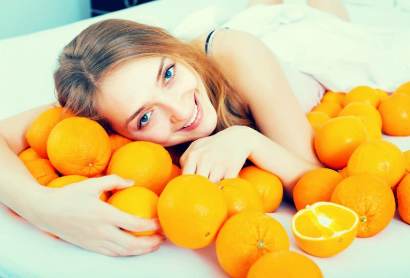 A young woman playfully curls up beside 20-plus oranges