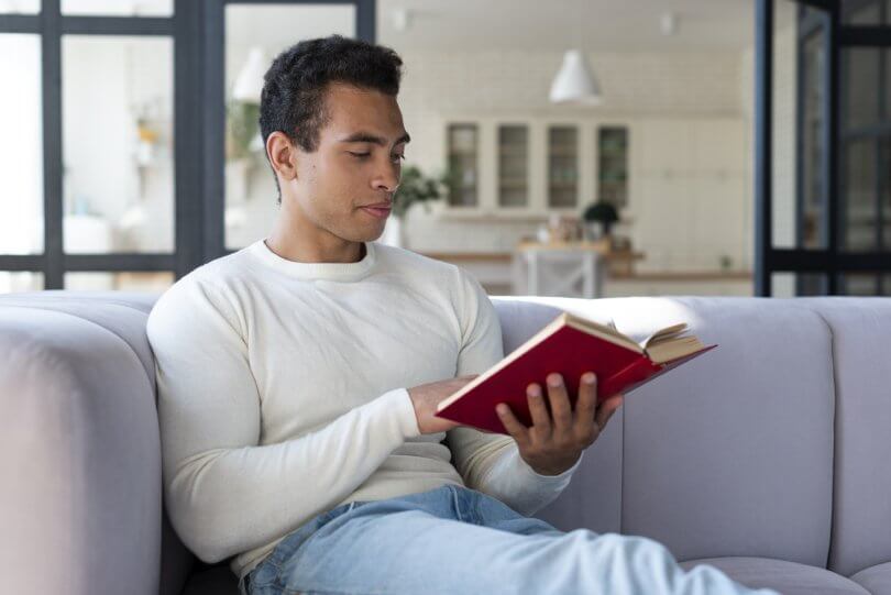 How to be successful on a raw vegan diet - man reading book on a couch - Fruit-Powered