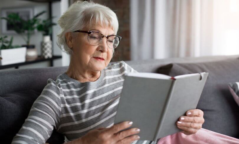 Proper sitting posture - elderly woman reading book on couch - Posture Exercises Method - Fruit-Powered